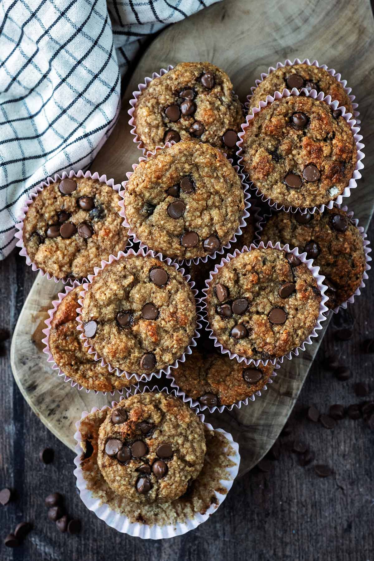 Twelve chocolate chip muffins on a wooden board.