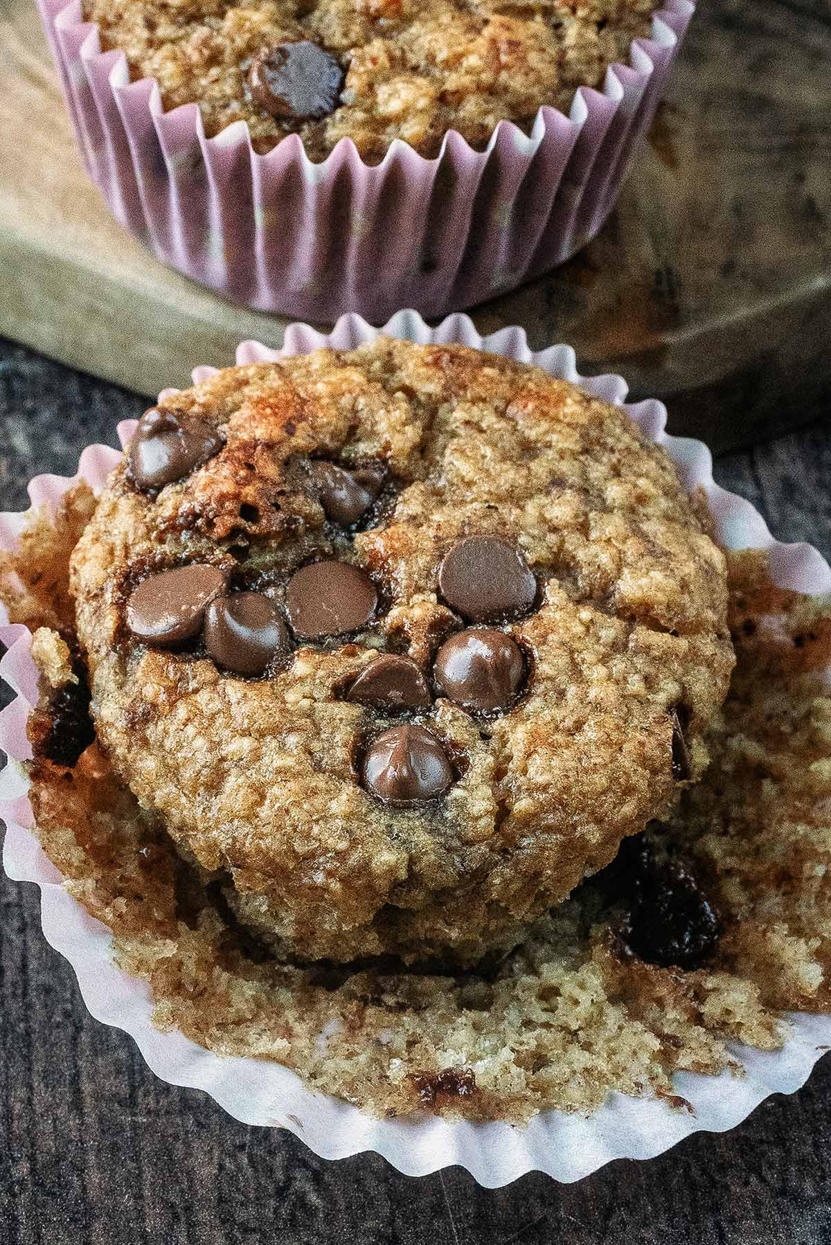 A chocolate chip banana muffin with its paper case pulled open.