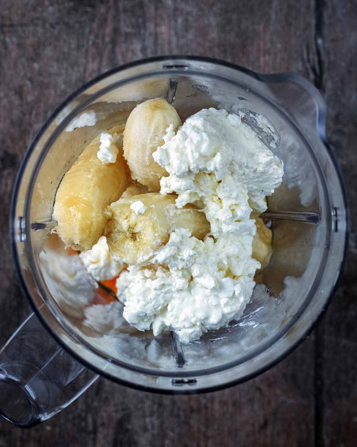 A blender jug containing banana, cottage cheese and maple syrup.