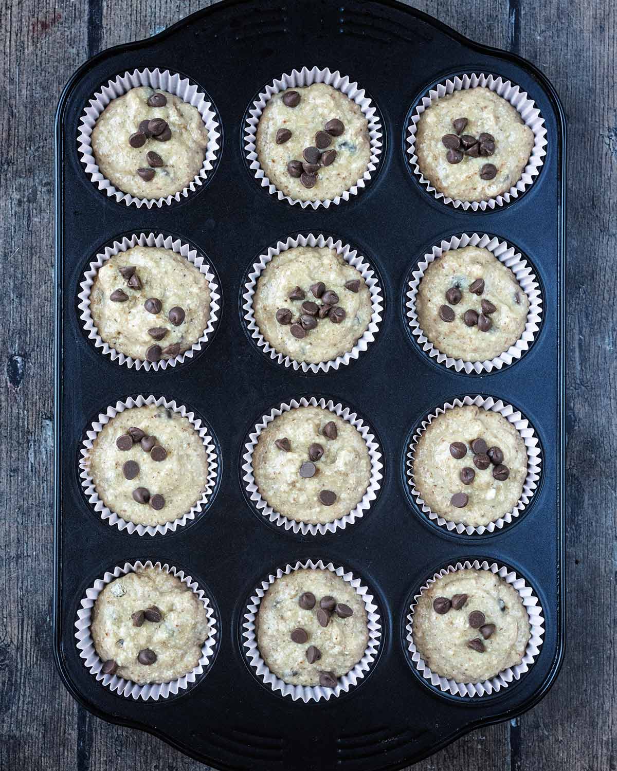 The batter poured into twelve muffin cases in a muffin tin.