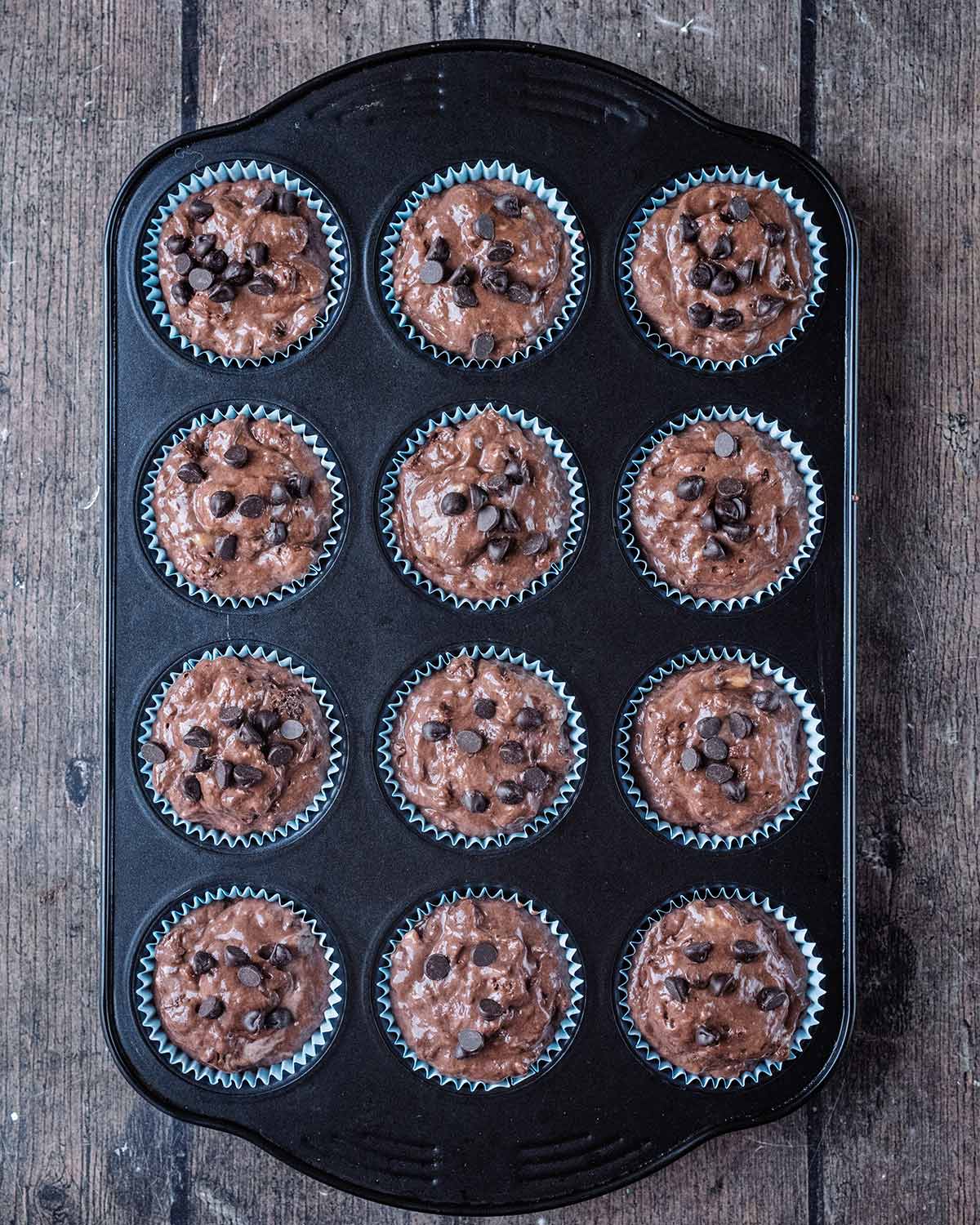 Twelve muffin cases filled with chocolate muffin batter in a muffin tin.