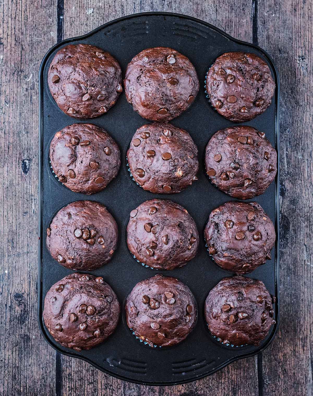 Twelve cooked chocolate muffins in the muffin tin.