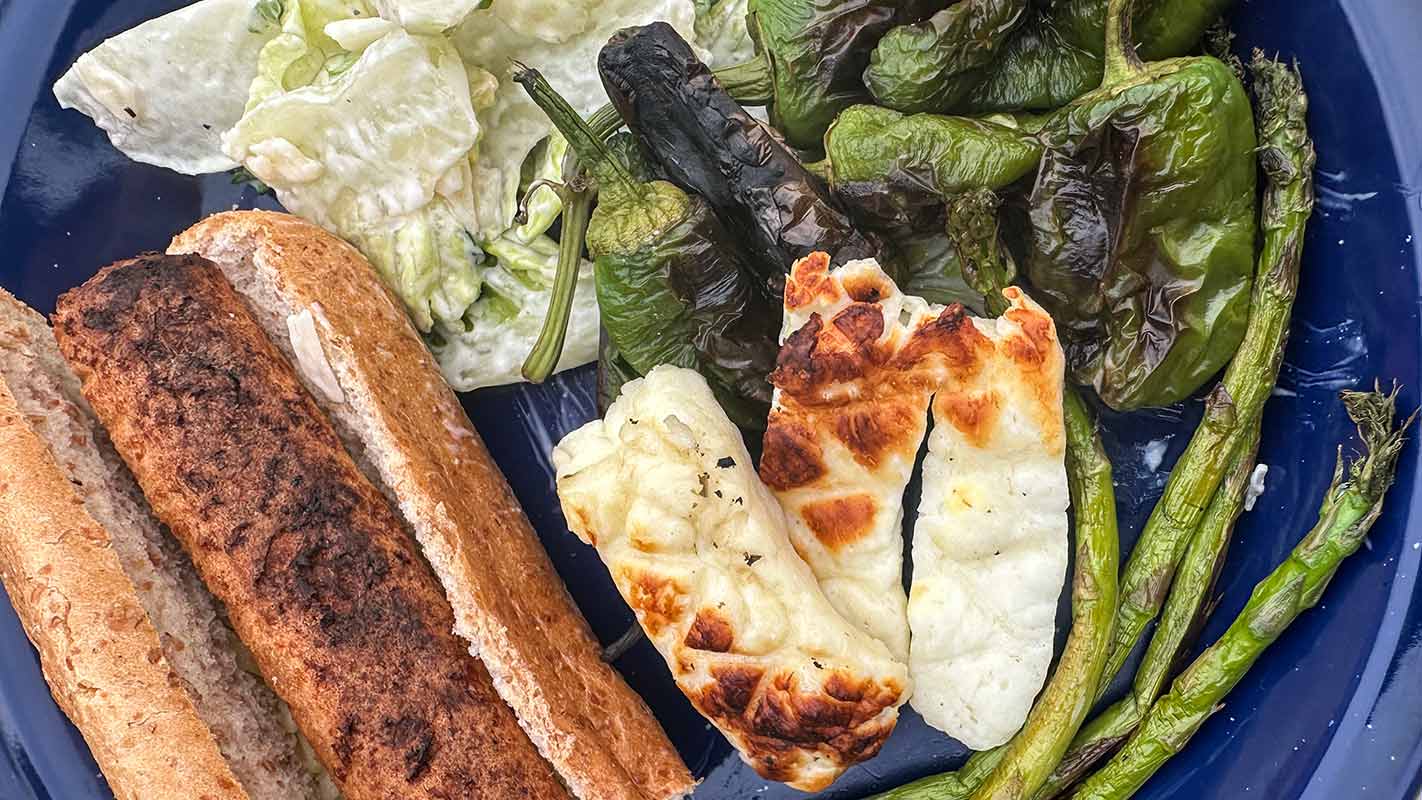 A hot dog, grilled halloumi, peppers, asparagus and salad on a blue plate.
