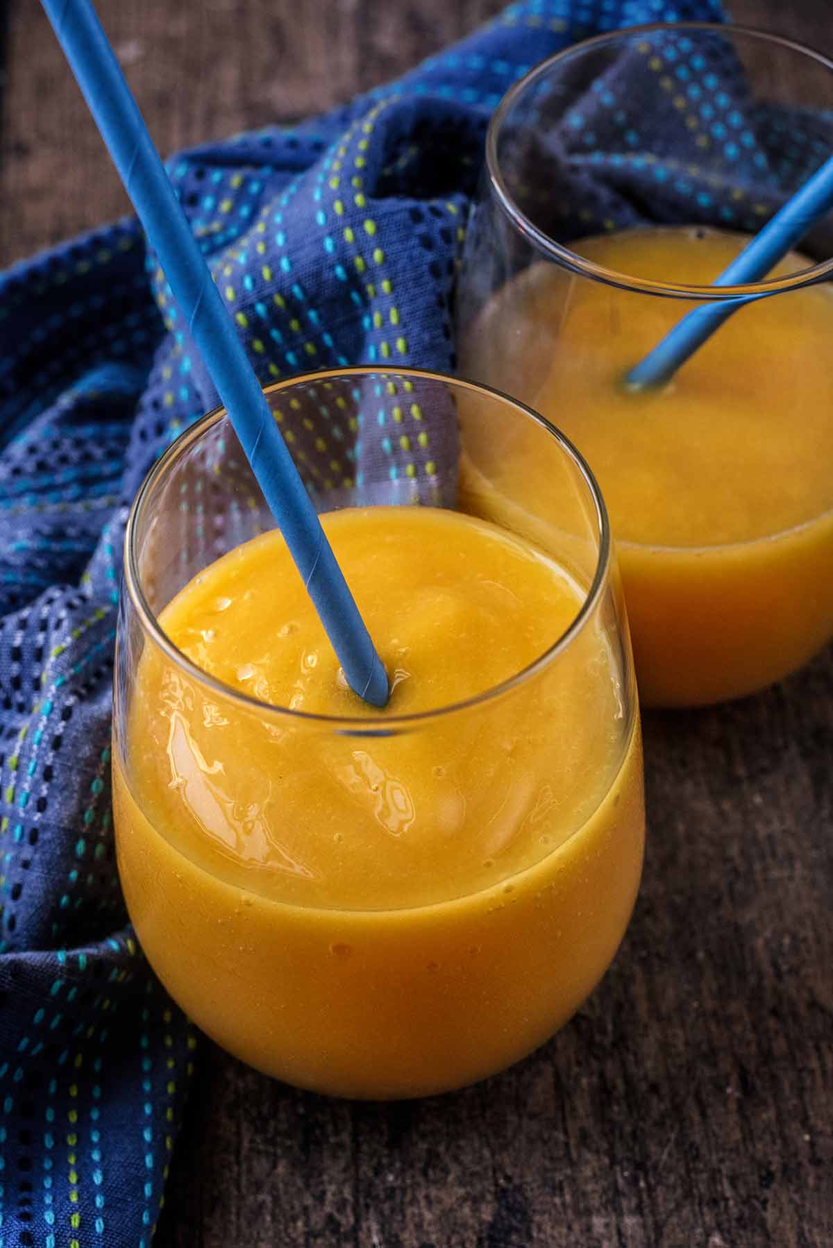 Two glasses of mango cooler each with a blue straw.