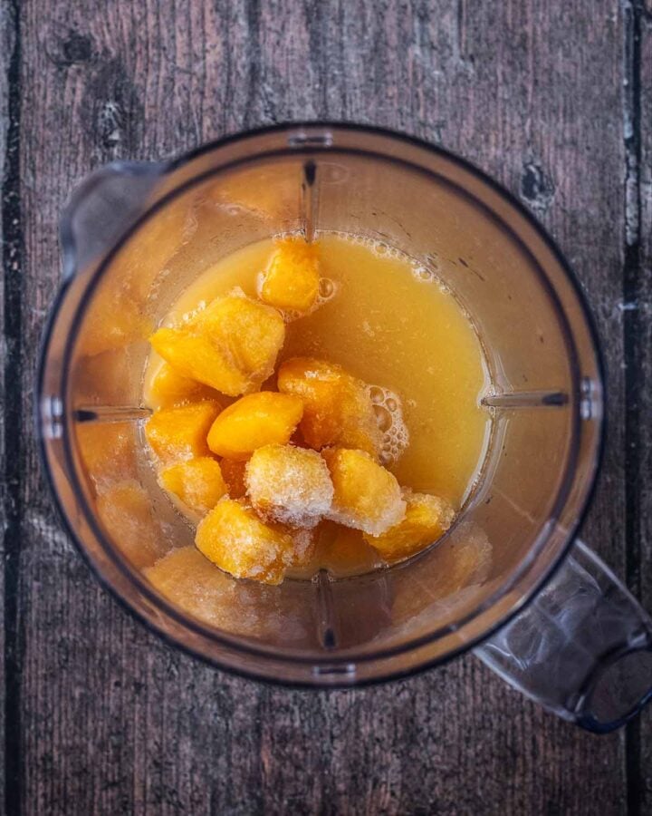 A blender jug containing chunks of frozen mango and passionfruit juice.