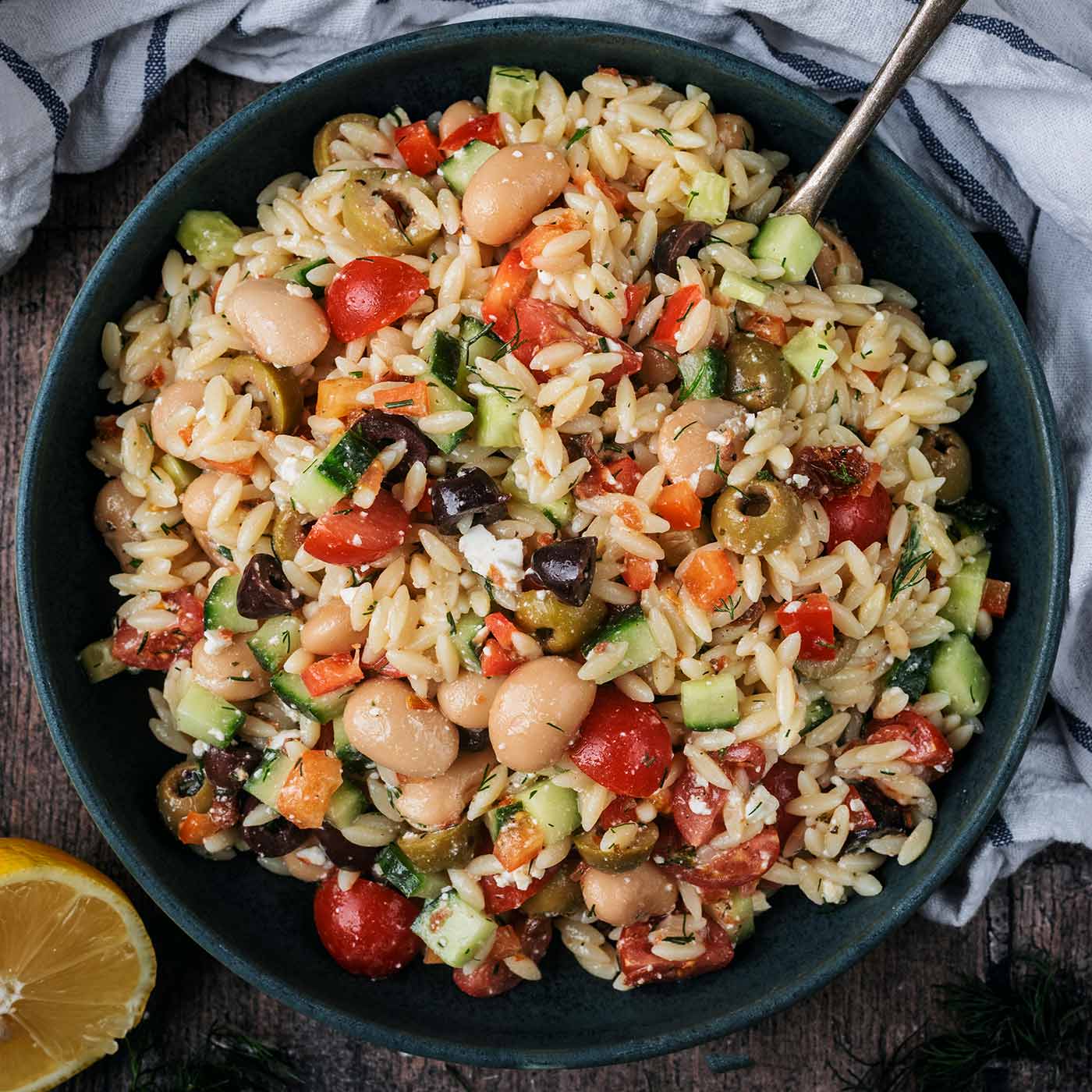 A large bowl of orzo pasta salad with a spoon in it.