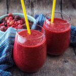 Red berry cooler in two glasses with yellow straws in each.