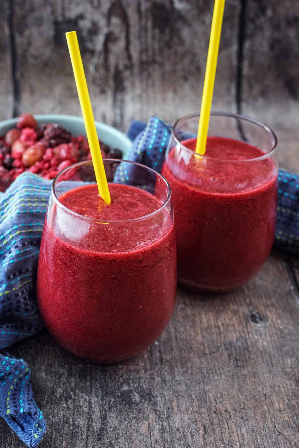 Two glasses of a thick, red drink, each with a straw in them.