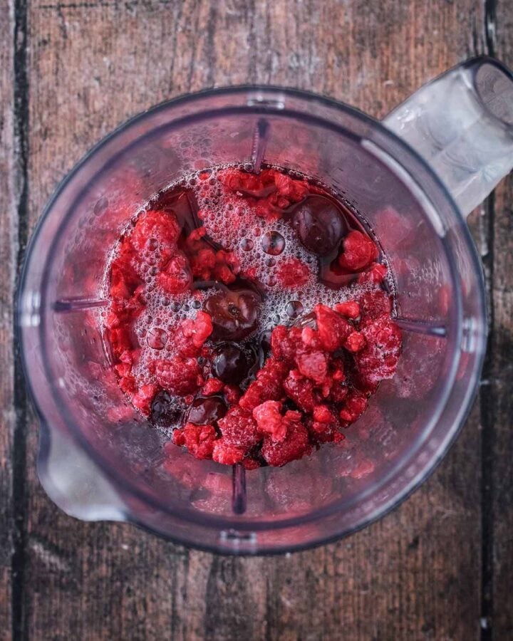 A blender jug containing frozen berries and fruit juice.