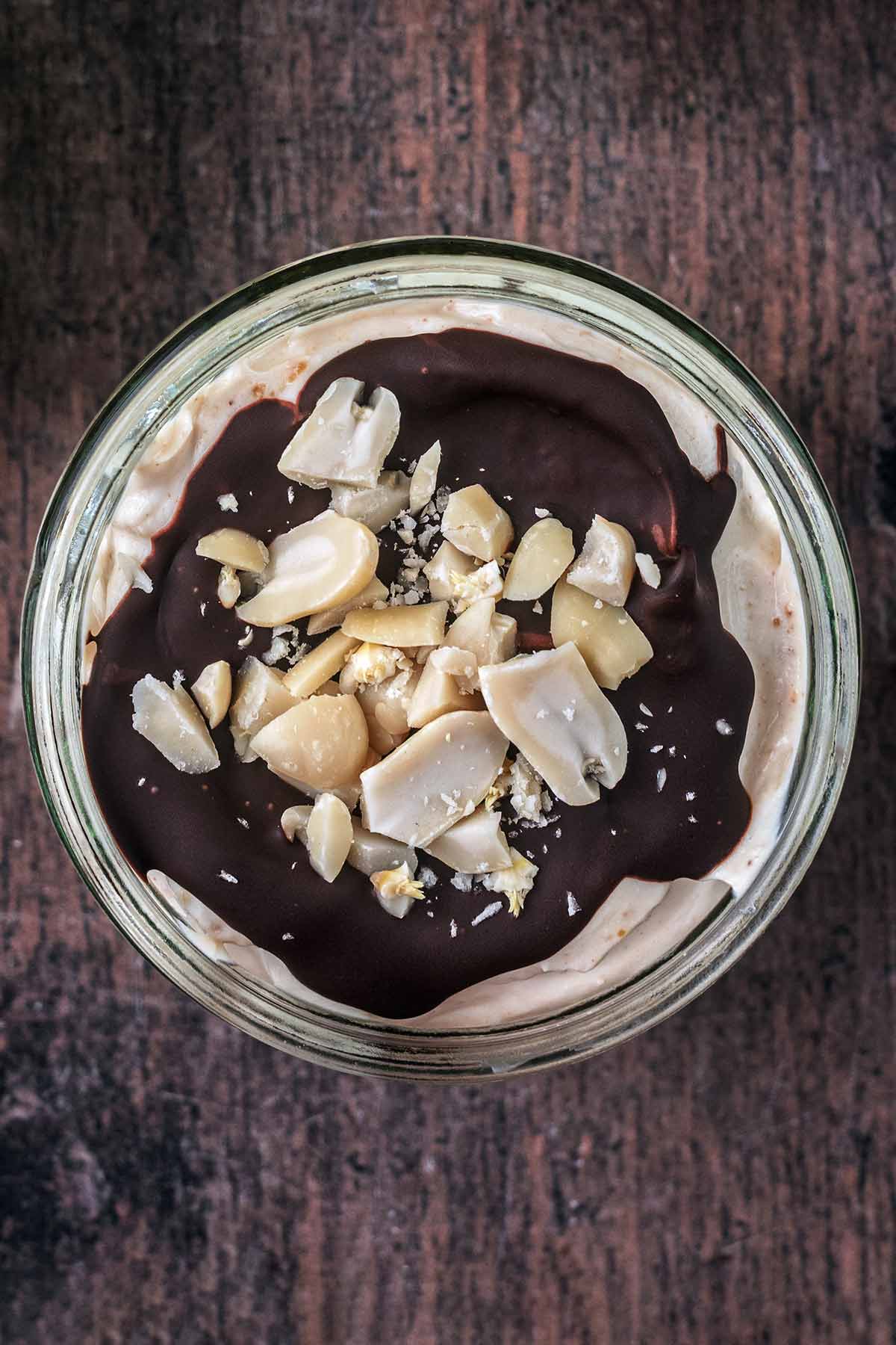 A ramekin of yogurt topped with a layer of chocolate and chopped peanuts.