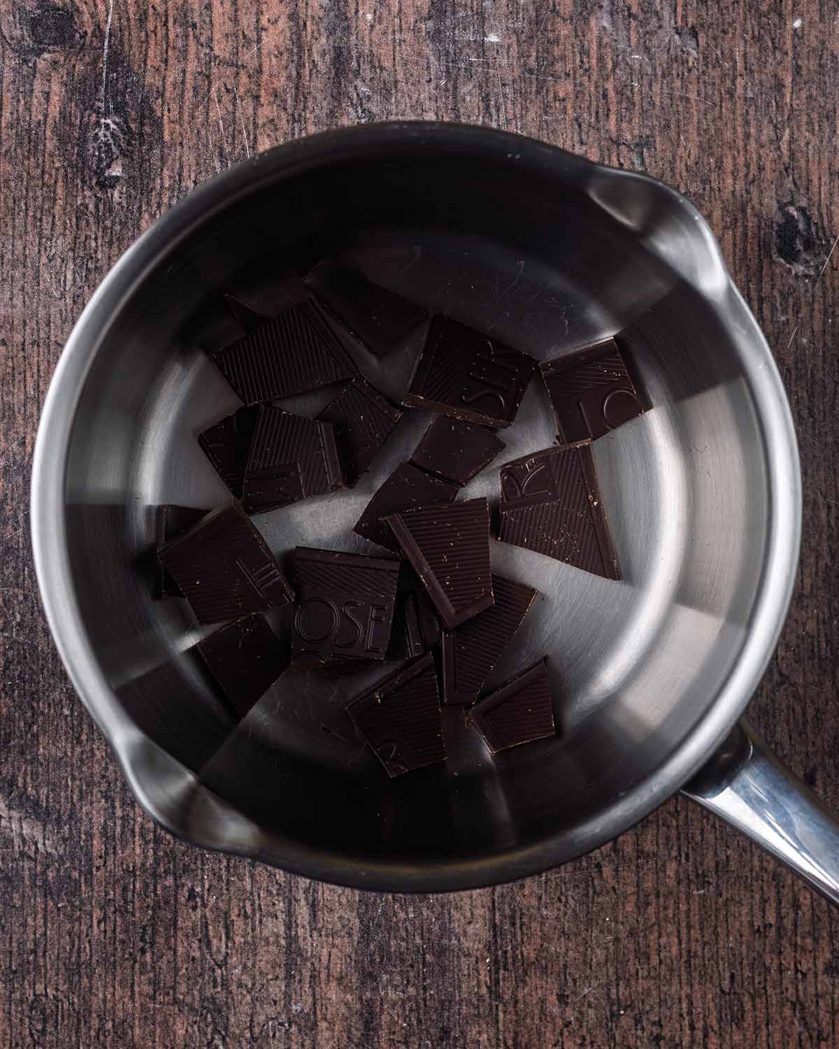 Shards of dark chocolate in a small silver saucepan.