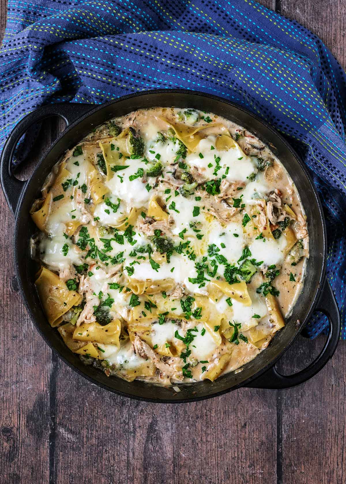 One pan lasagna on a wooden surface next to a blue towel.