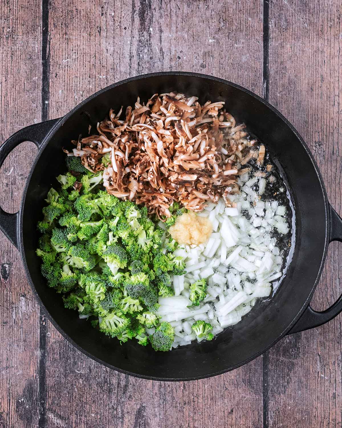Chopped onion, grated mushroom, broccoli florets and garlic cooking in a pan.