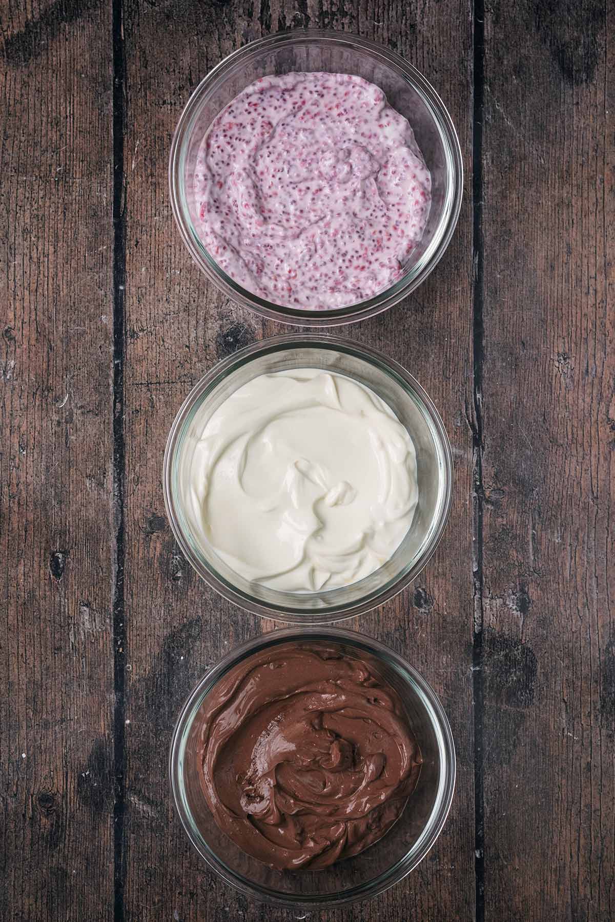 A bowl of raspberry yogurt, a bowl of vanilla yogurt and a bowl of chocolate yogurt.