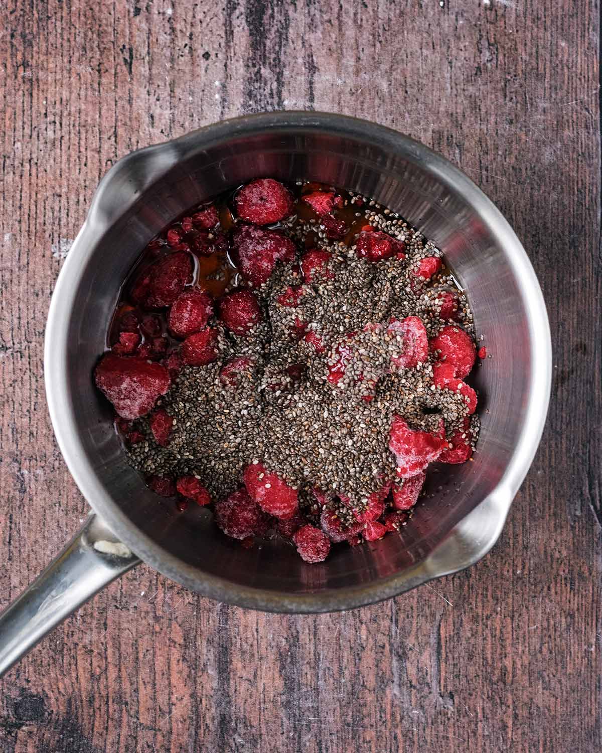 A saucepan containing raspberries, maple syrup and chia seeds.