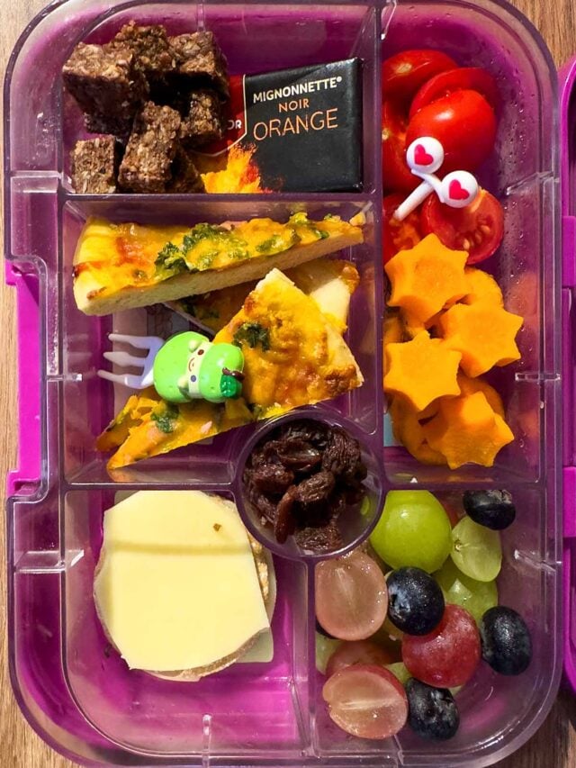 A compartment lunchbox containing pizza slices, carrot stars, grapes and chocolate.