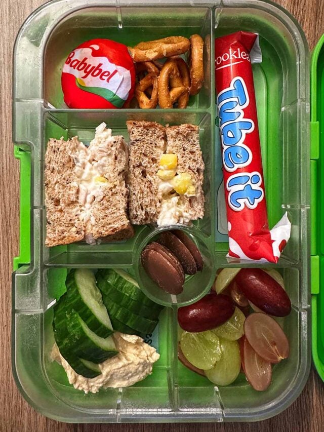 A compartment lunchbox containing a tuna mayo sandwich, cucumber, hummus, grapes, Babybel and a Frube yogurt.