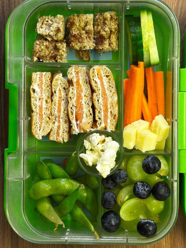 A compartment lunchbox containing a sandwich, edamame, carrots, cheese and a flapjack.