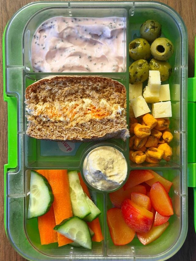 A compartment lunchbox containing a sandwich, olives, yogurt, carrot, cucumber, olives and corn.