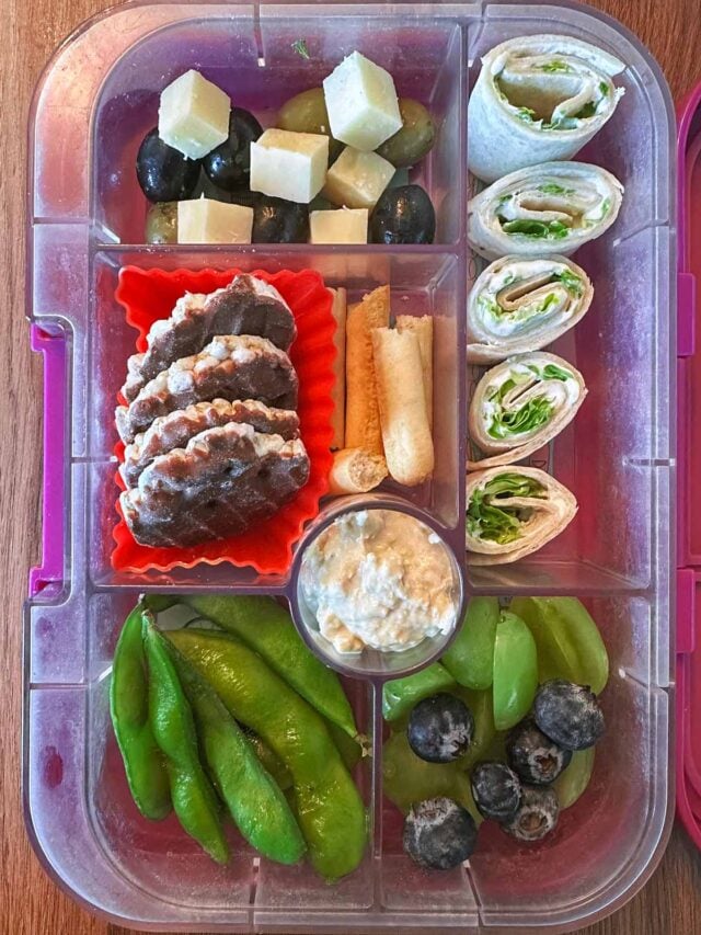 A compartment lunchbox containing wraps, edamame, berries, cheese and rice cakes.
