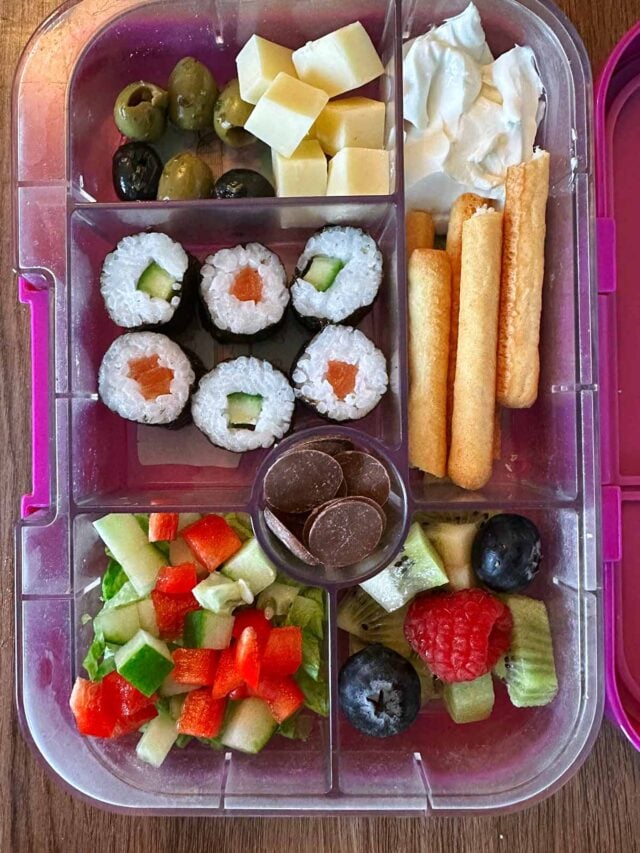A compartment lunchbox containing sushi, salad, breadsticks and berries.