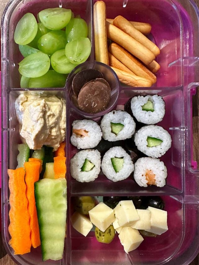 A compartment lunchbox containing sushi, fruit, veg, cheese and hummus.