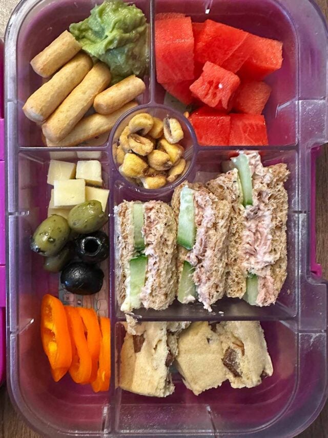 A compartment lunchbox containing a sandwich, breadsticks, guacamole, watermelon and a cookie.