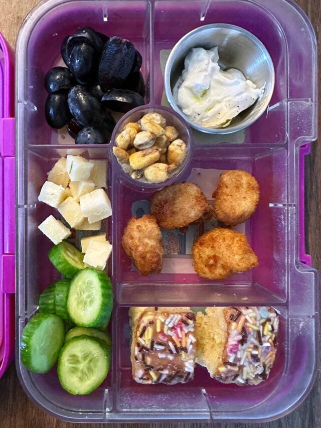 A compartment lunchbox containing breaded chicken, cheese, olives, cucumber and school cake.
