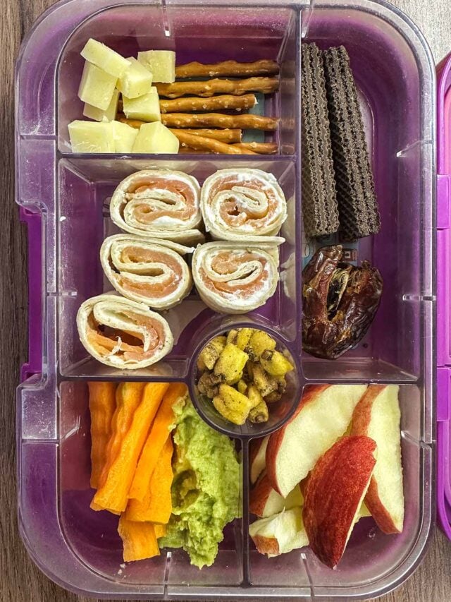 A compartment lunchbox containing pinwheels, fruit and chocolate wafers.