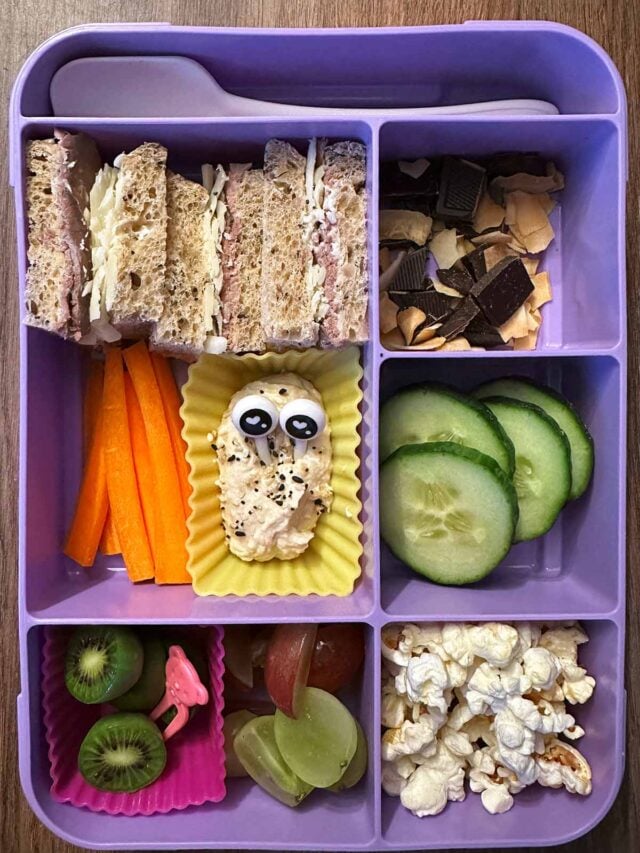 A compartment lunchbox containing a sandwich, fruit and veg, popcorn and chocolate.