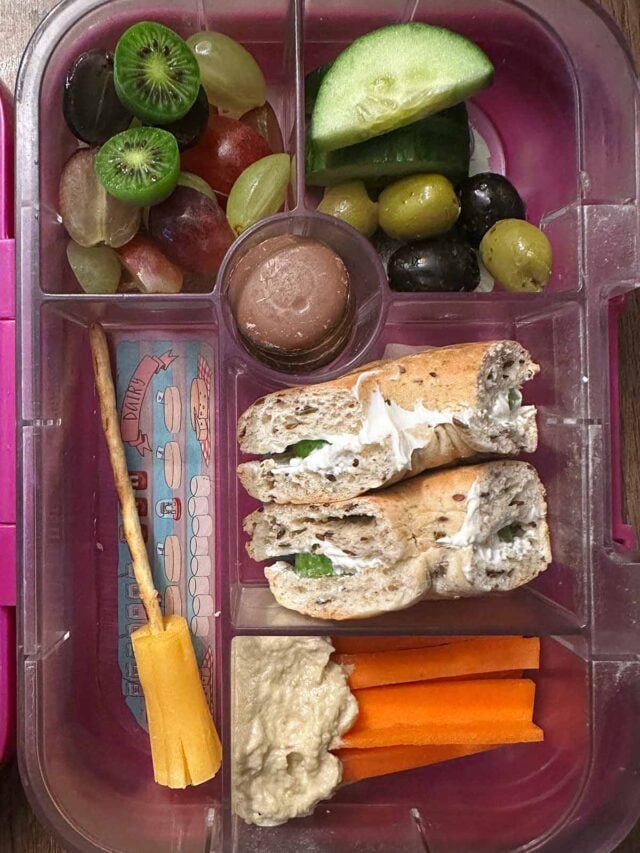 A compartment lunchbox containing a bagel, carrot sticks, fruit, veg and chocolate.