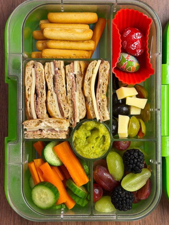 A compartment lunchbox containing a sandwich, fruit, veg, breadsticks, guacamole and chocolate mini eggs.
