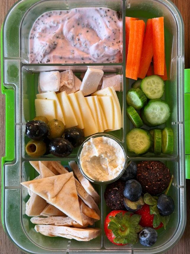 A compartment lunchbox containing cheese, pitta chips, chicken, fruit, veg, yogurt and energy balls.