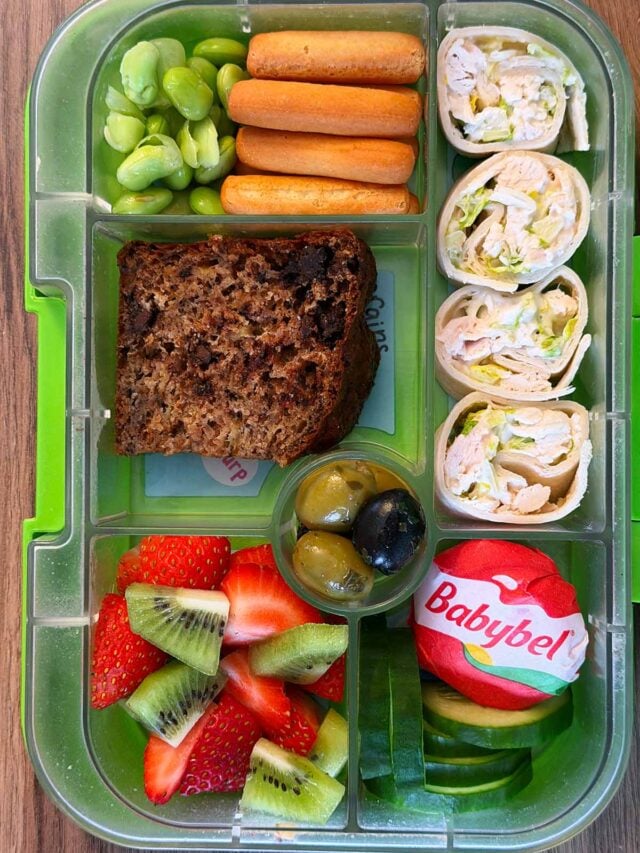 A compartment lunchbox containing wrap, banana bread, cheese, berries, breadsticks and edemamae.