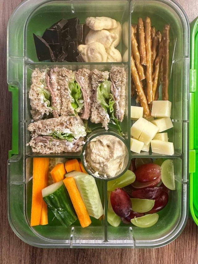 A compartment lunchbox containing a sandwich, fruit, veg, pretzel sticks, cheese, chocolate and biscuits.