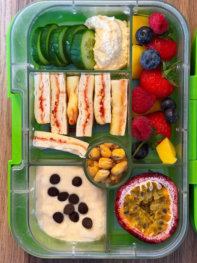 A compartment lunchbox containing pizza bites, berries, cucumber, hummus, passionfruit and rice pudding.
