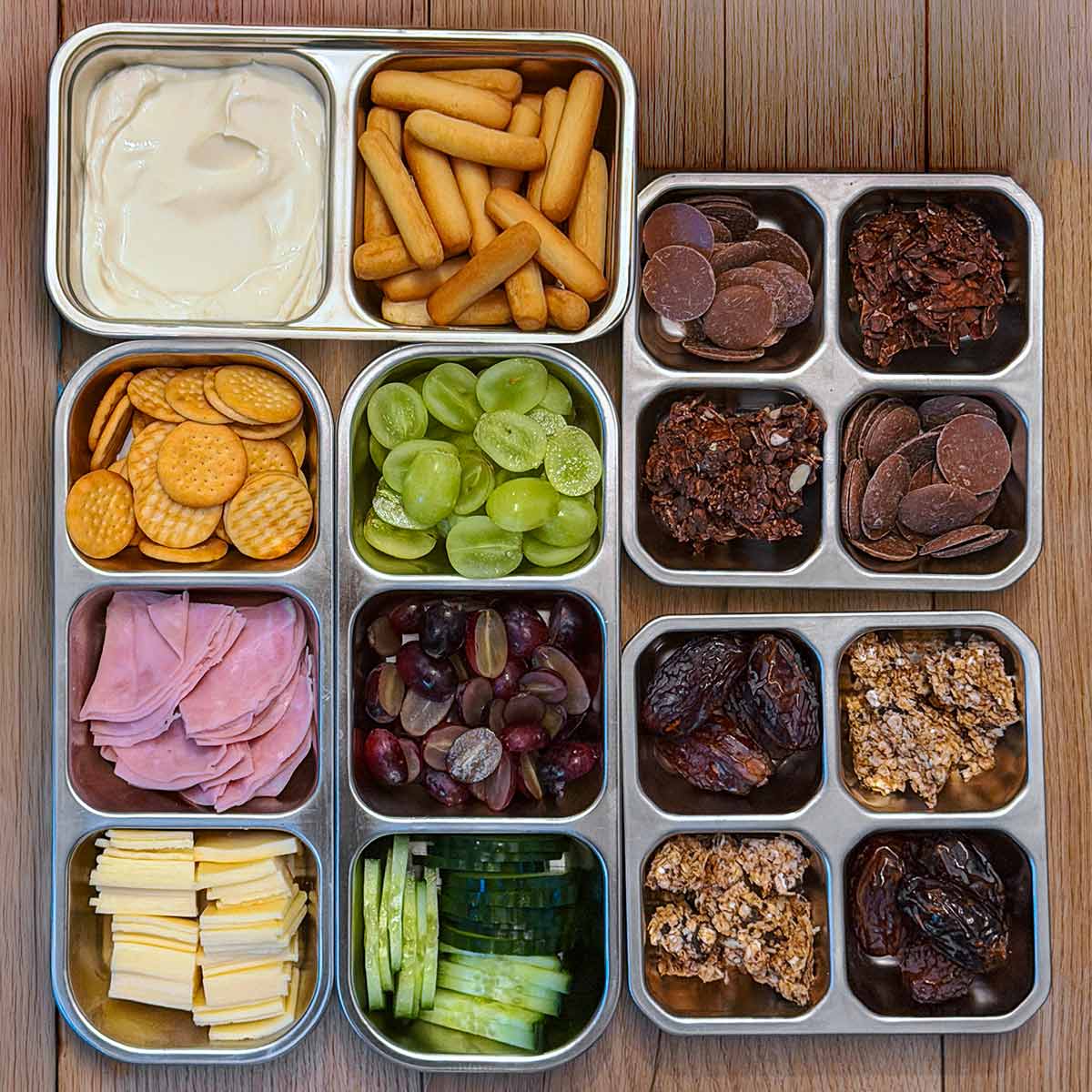 A selection of five metal food containers all filled with different snacks.