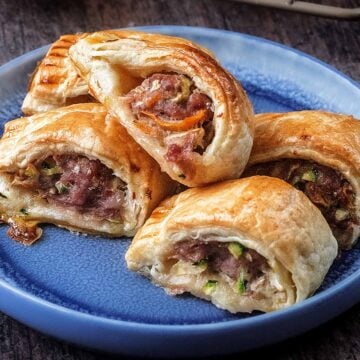 Five sausage rolls with vegetables on a blue plate.