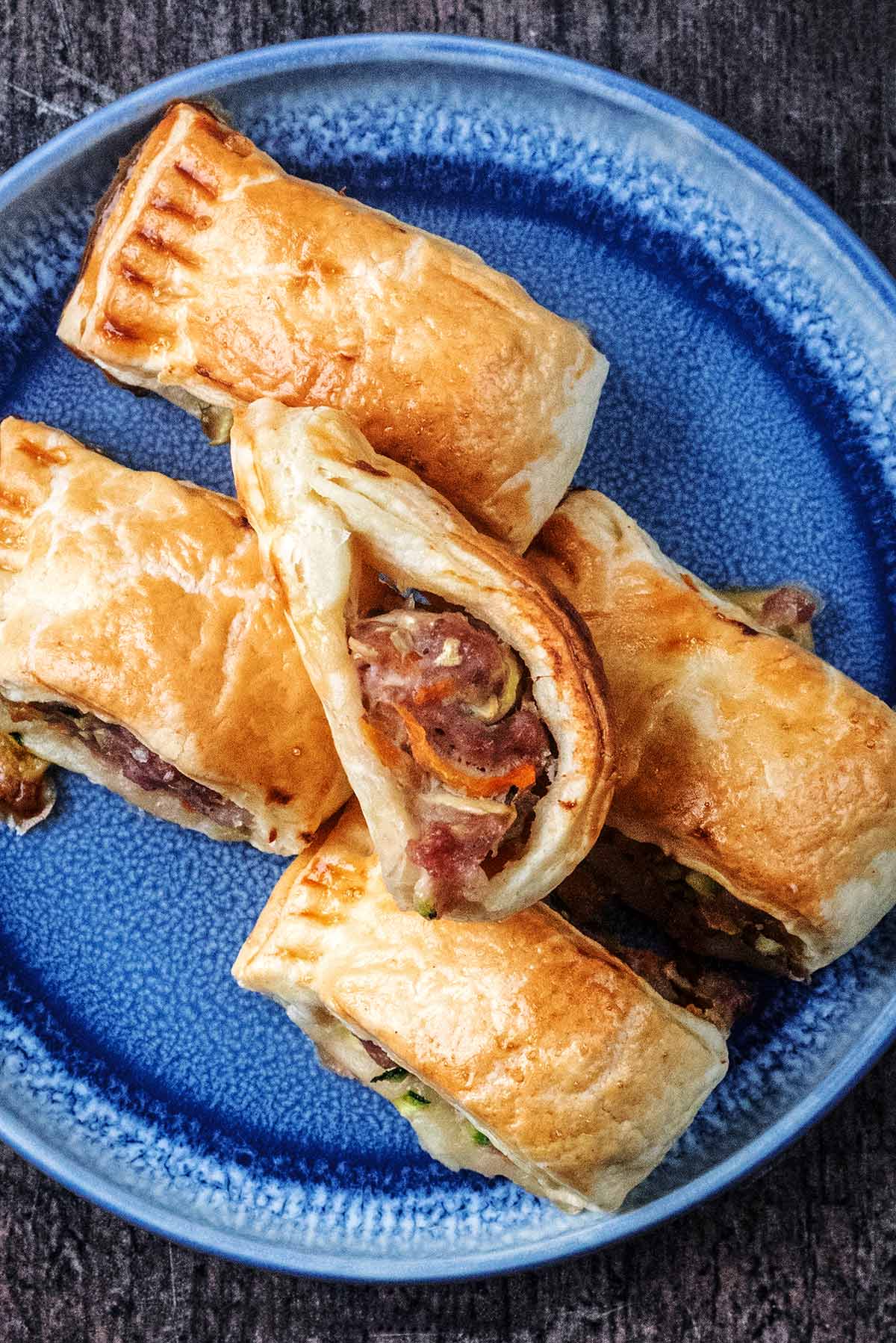 Five mini sausage rolls on a blue plate.