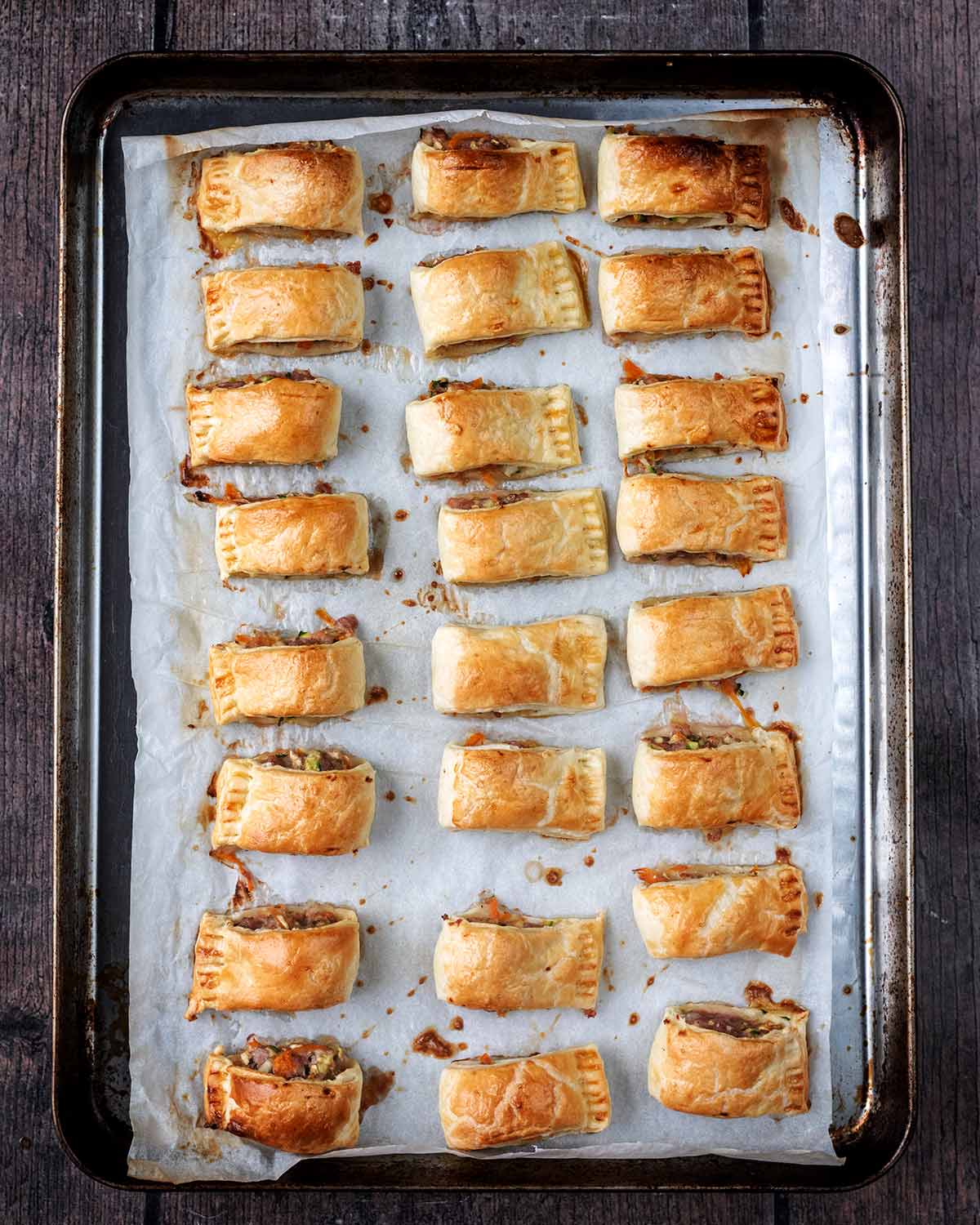 Twenty four baked sausage rolls on the baking tray.