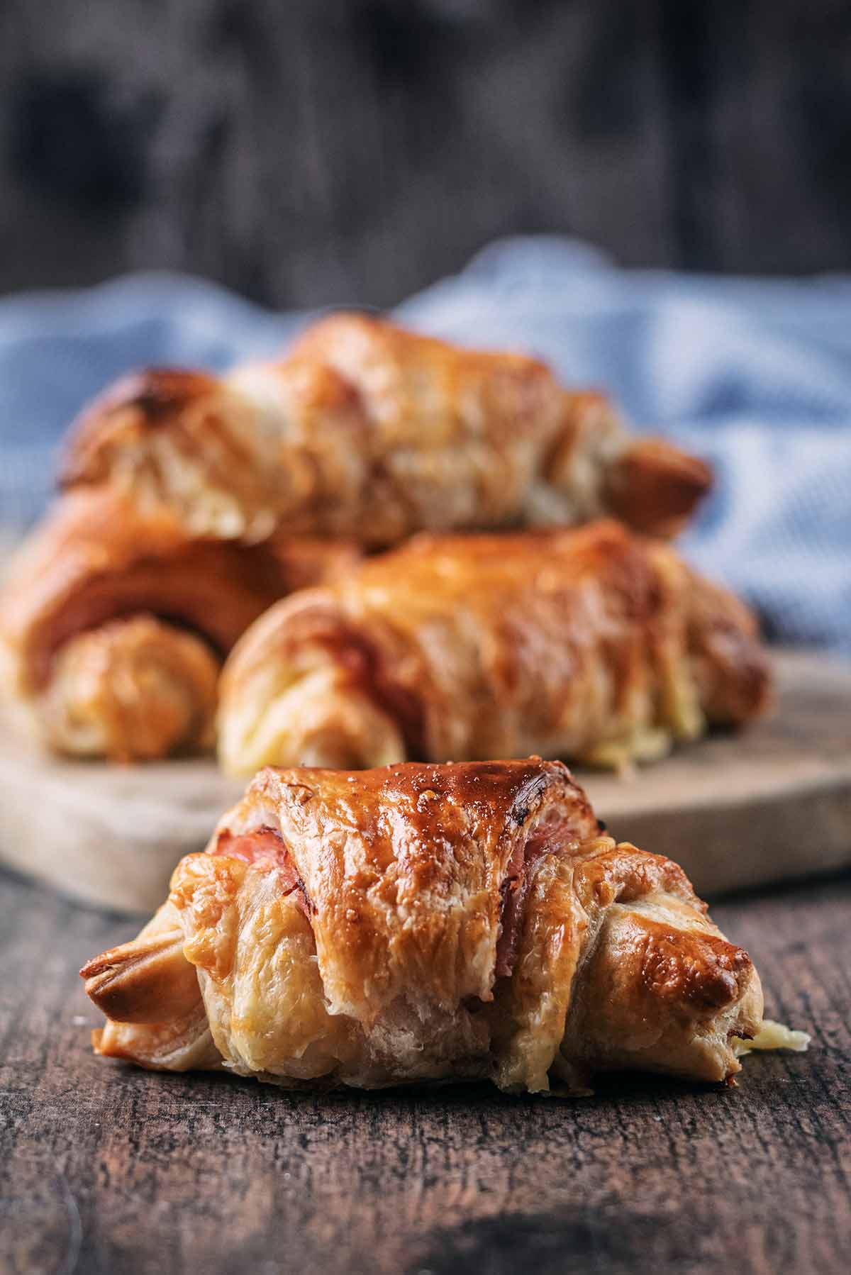 A ham and cheese croissant with more croissants in the background.