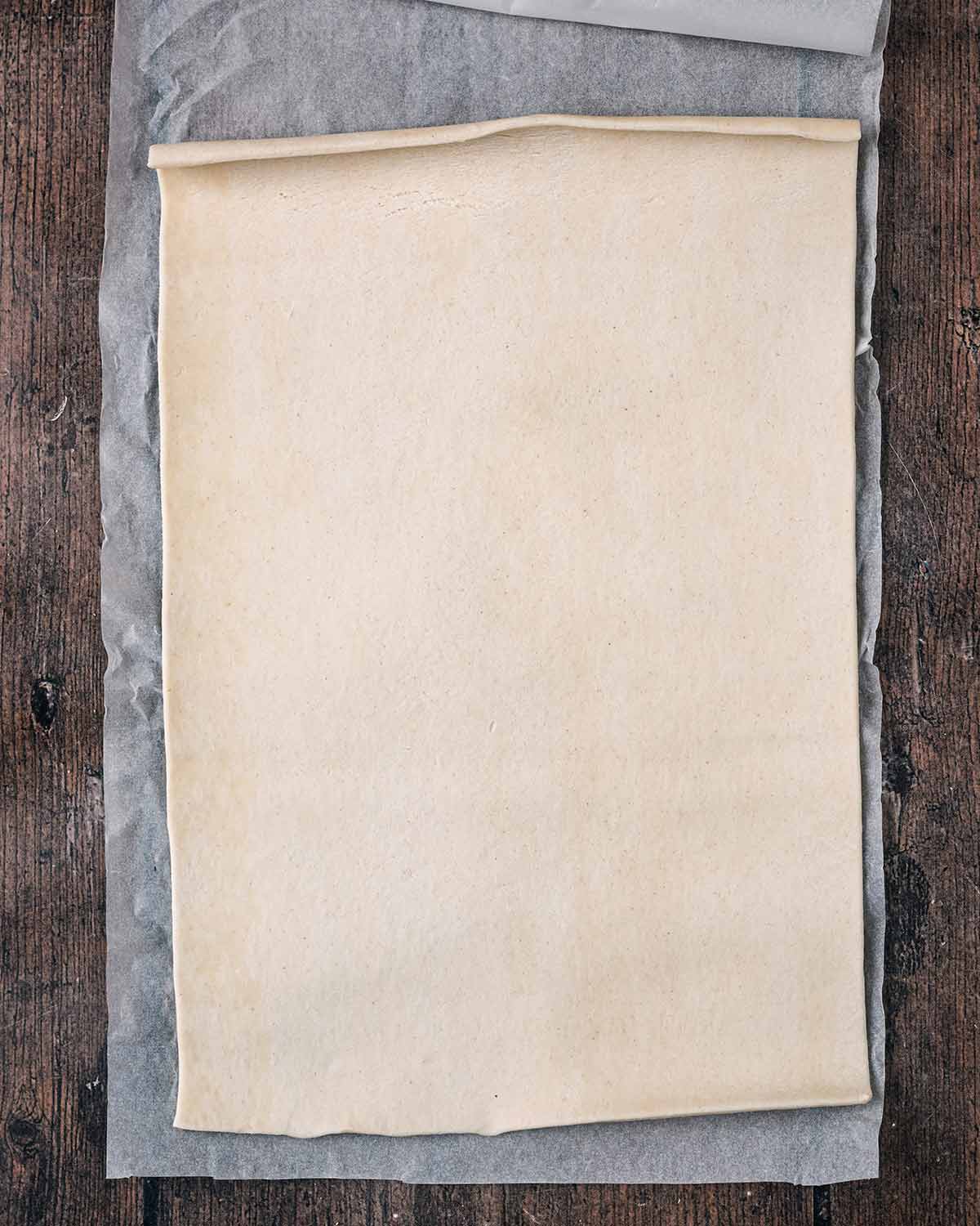 A sheet of puff pastry rolled out on some baking paper.