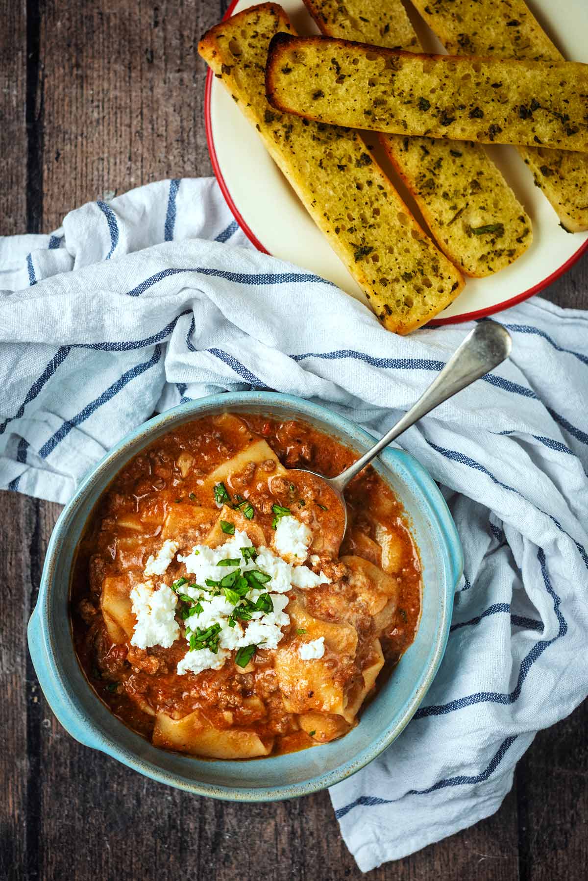 Lasagna soup in a bowl next to a plate of garlic bread.