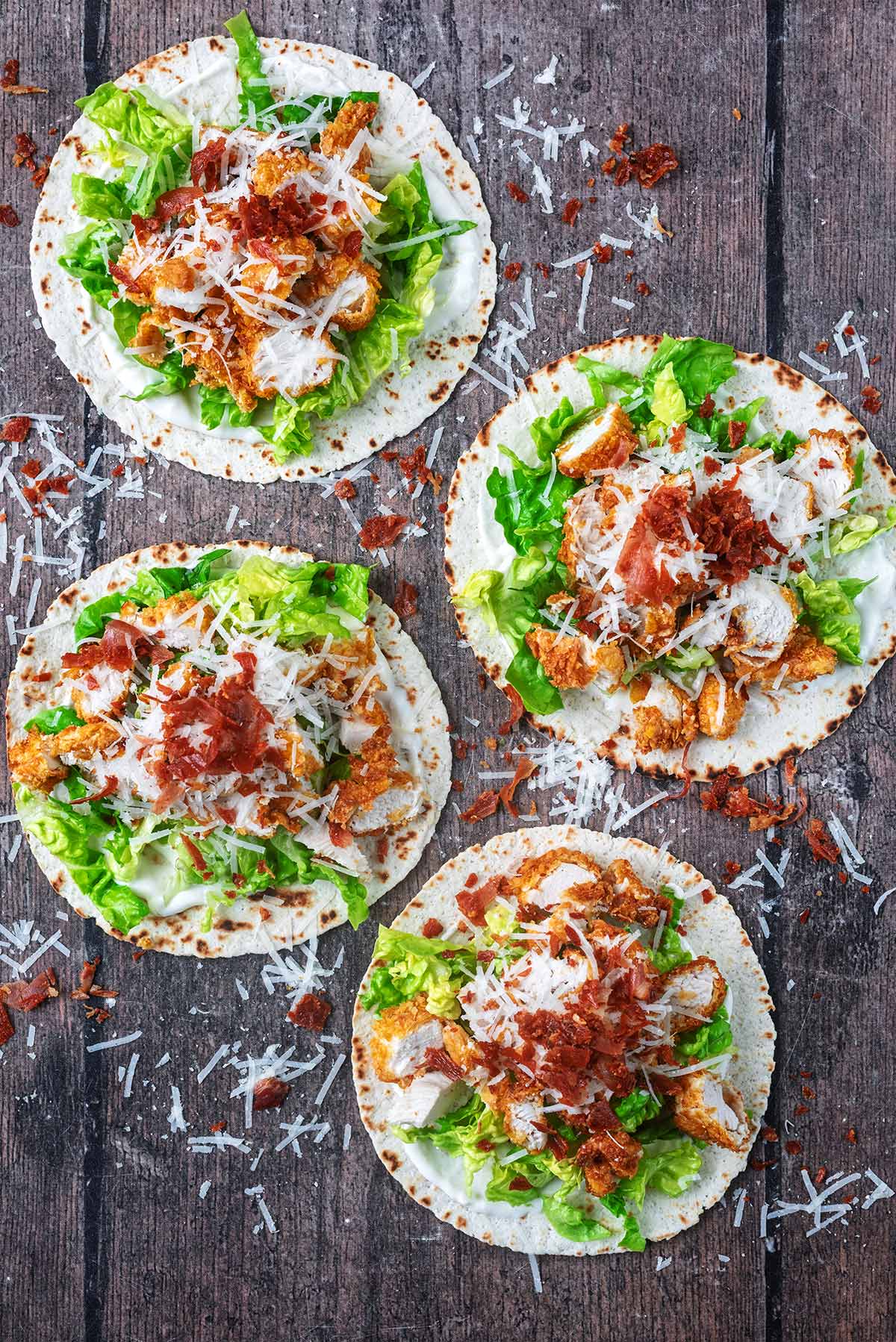 Four chicken caesar tacos on a wooden surface.