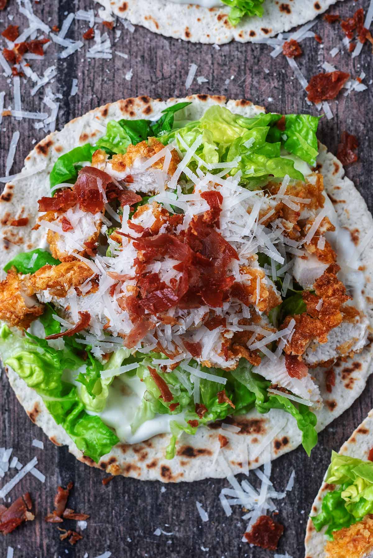 A taco made up of caesar dressing, lettuce, cornflake chicken, Parmesan and crispy prosciutto.