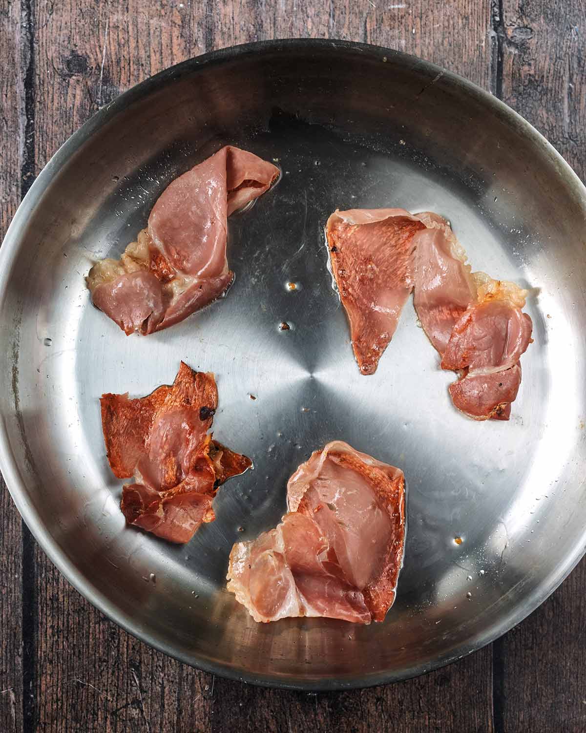 Four pieces of prosciutto cooking in a large pan.