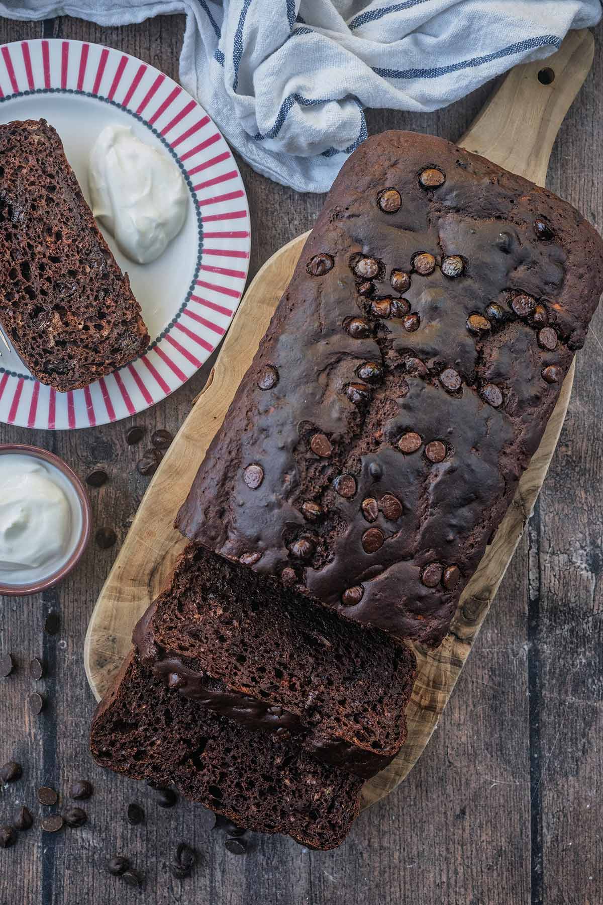 A long chocolate courgette cake on a wooden board with slices cut off.
