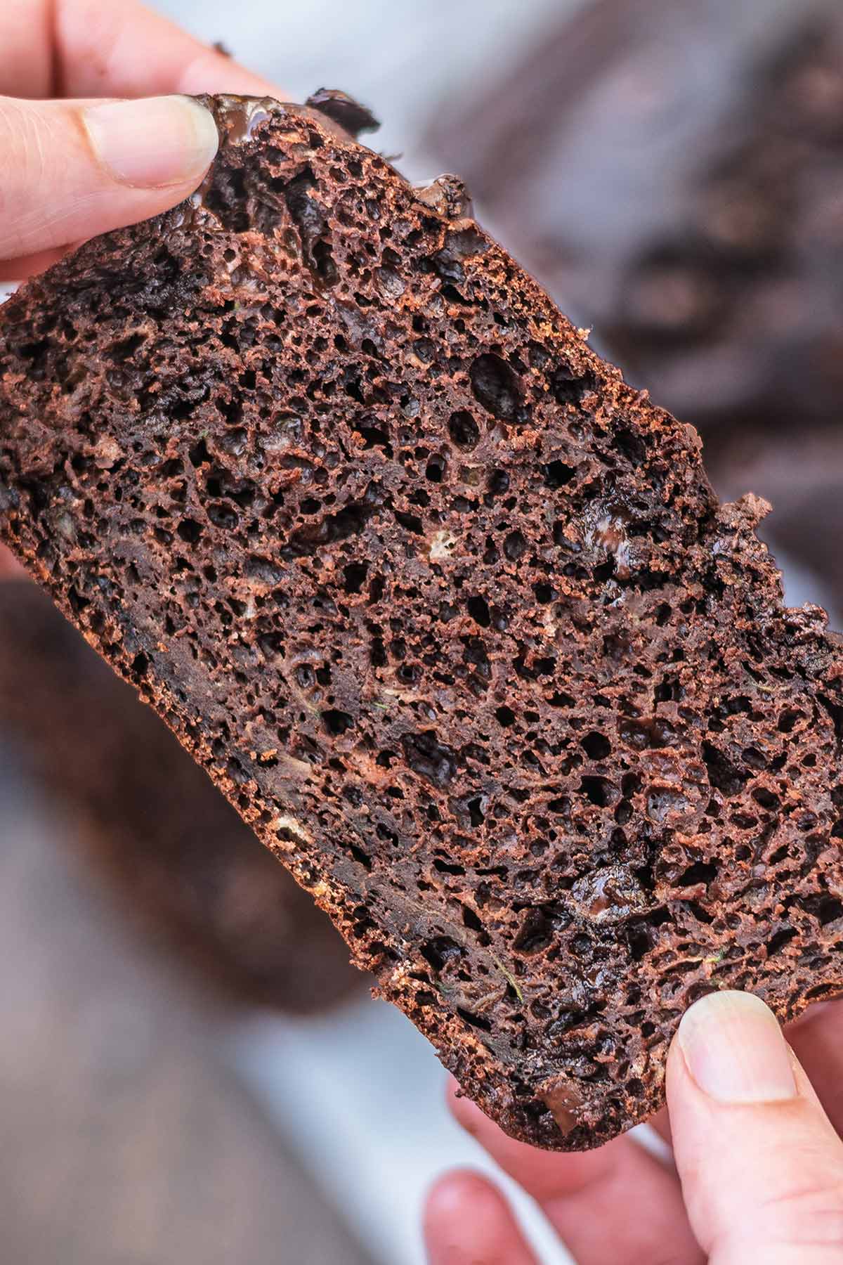 Hands holding a slice of chocolate loaf cake showing the crumb of the cake.