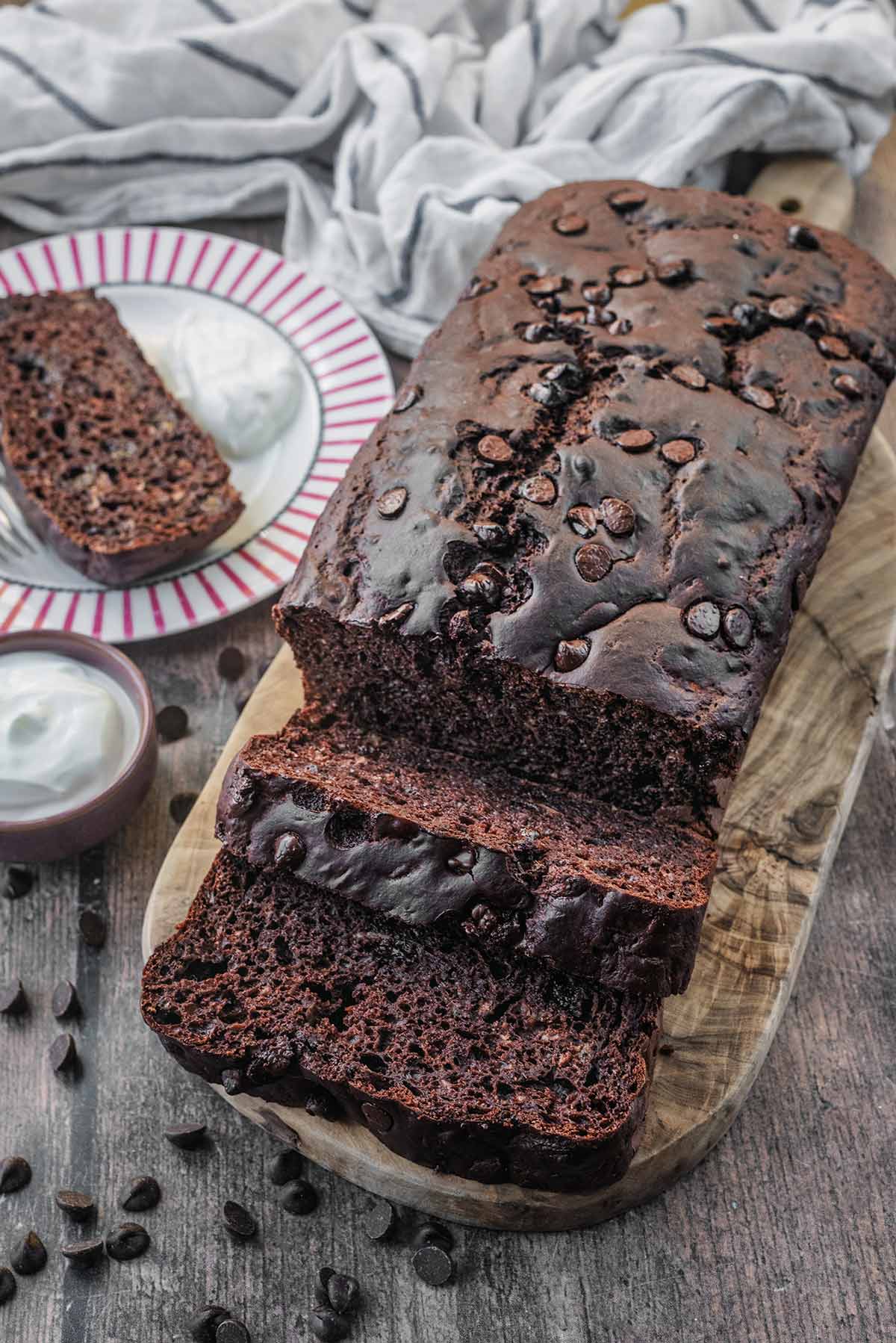 A chocolate loaf cake cut into slices with a slice on a small side plate.