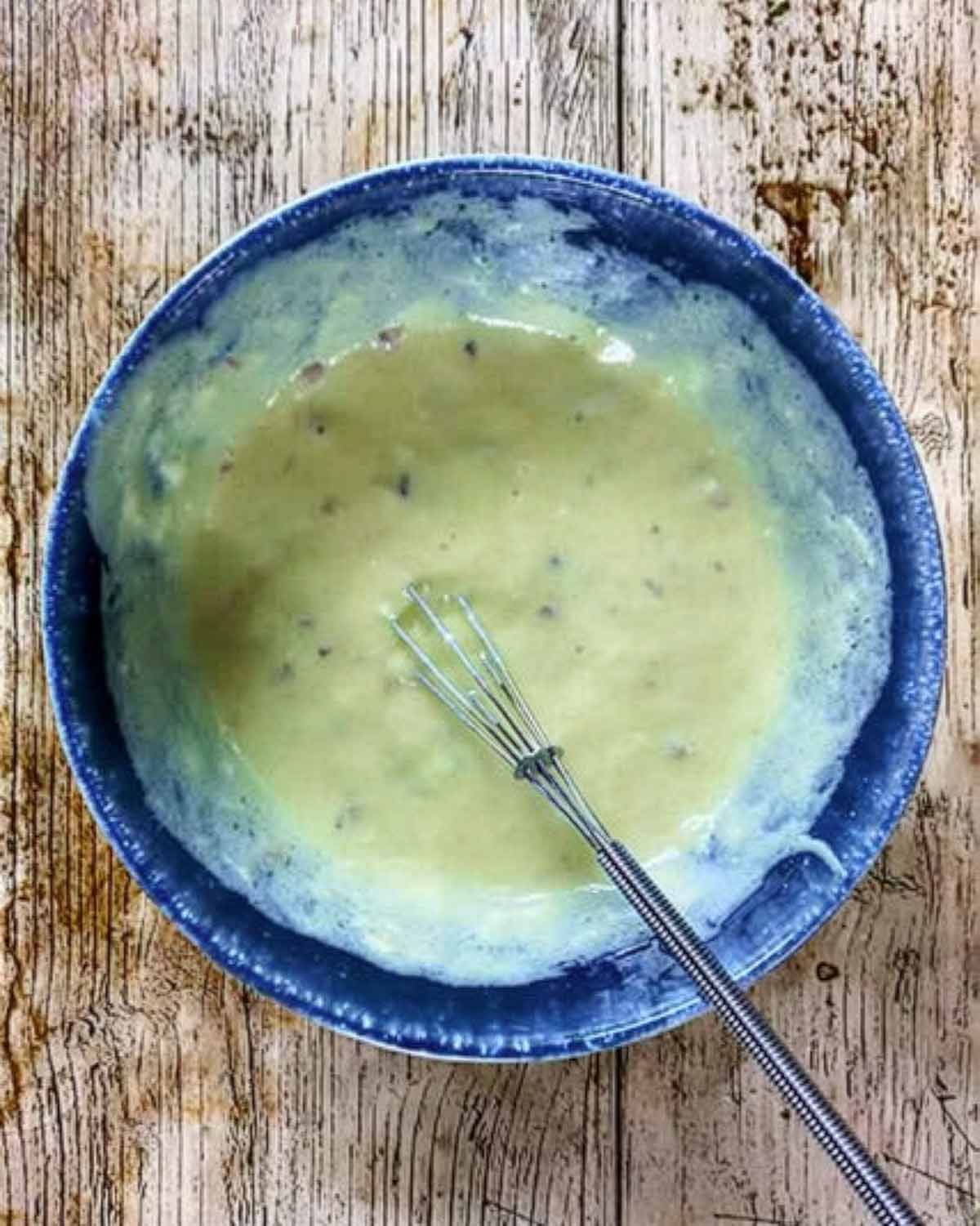 A bowl of healthy Caesar salad dressing with a small whisk.
